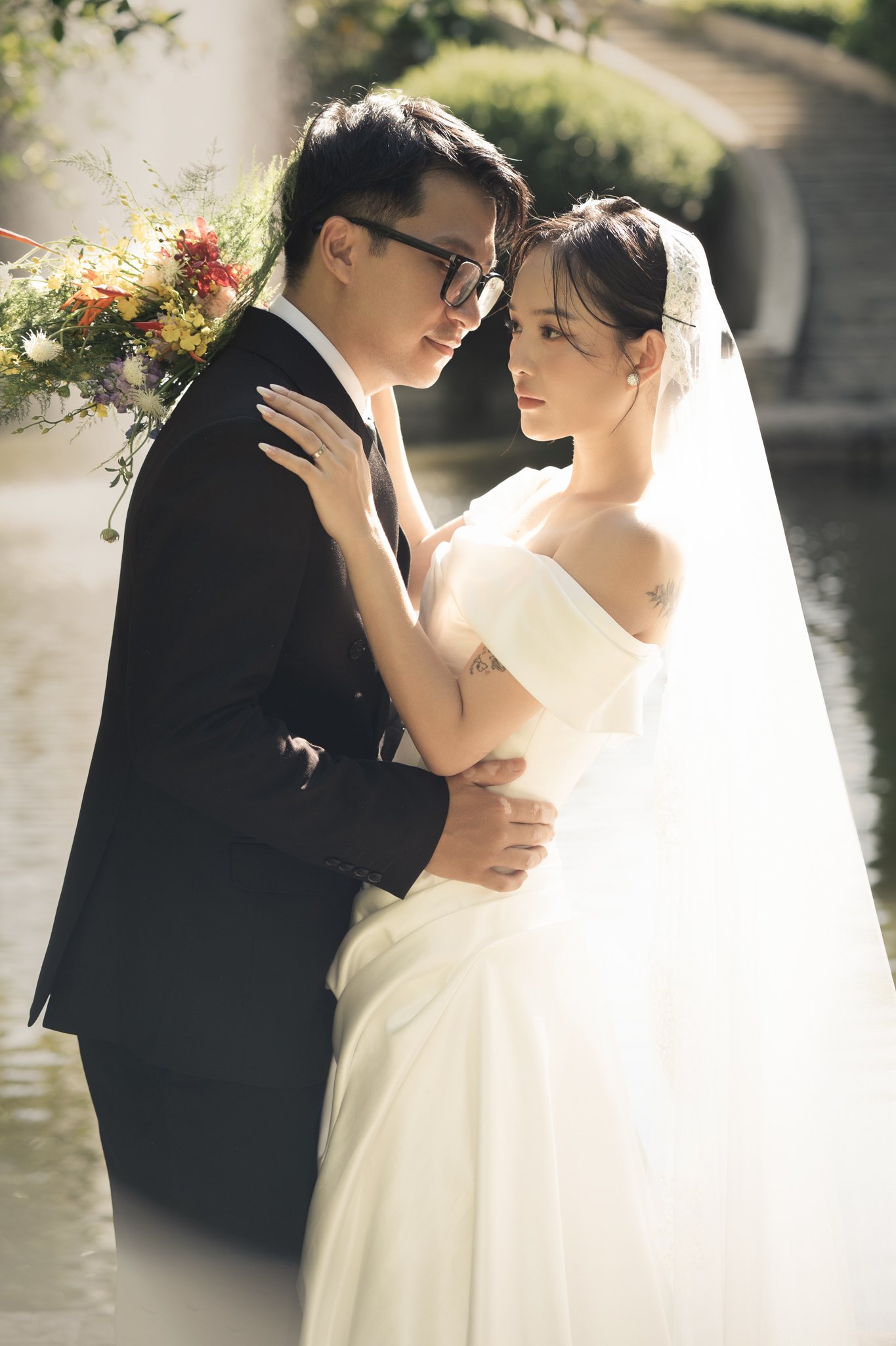 Cô dâu chú rể ôm nhau trong vườn, cô dâu trùm voan dài
